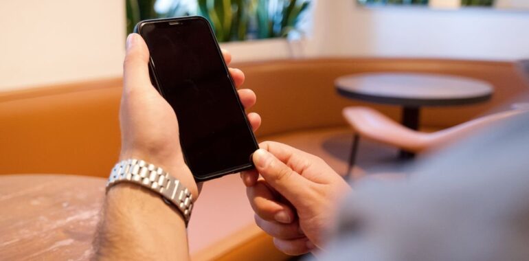 Personne consultant son téléphone dans un café, illustrant un agent IA pour les avis Google qui prépare les réponses aux clients