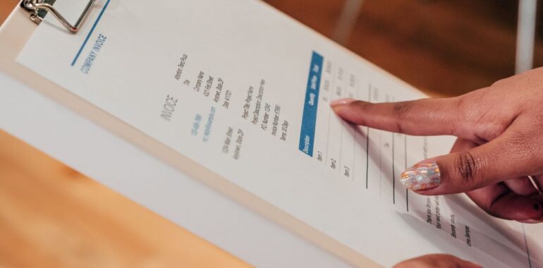 Main qui pointe une ligne sur une facture d'entreprise tenue sur une planchette