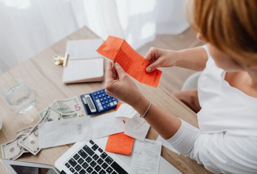 Femme qui examine un reçu à son bureau, entourée de factures, d'une calculatrice et d'un ordinateur portable