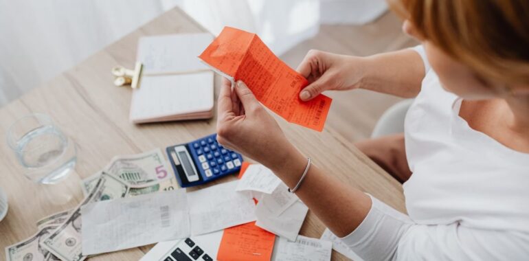 Femme qui examine un reçu à son bureau, entourée de factures, d'une calculatrice et d'un ordinateur portable
