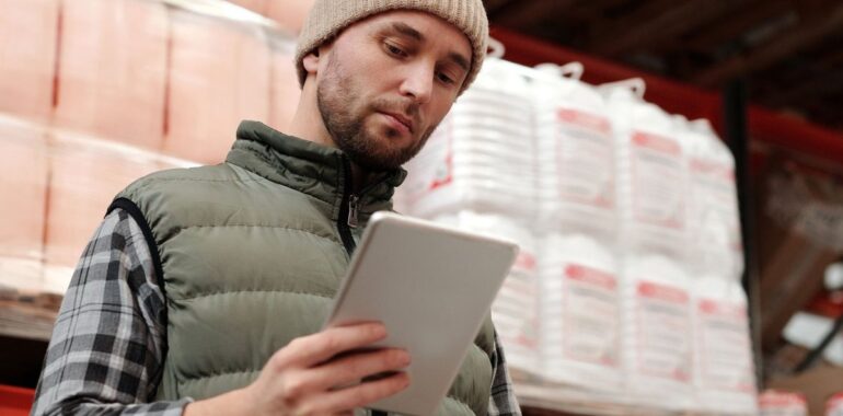 Employé d'entrepôt consultant une tablette devant des étagères, illustrant un agent IA pour l'inventaire dans une PME