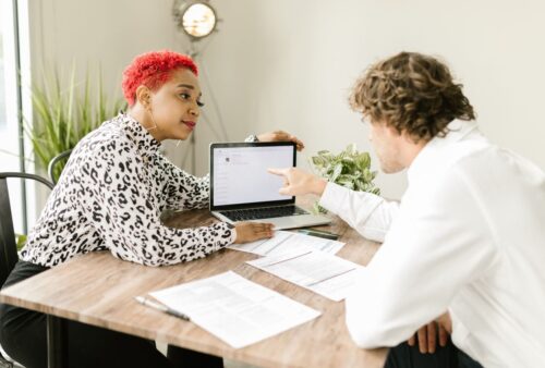 Deux collègues consultent un ordinateur portable et des documents sur une table de bureau