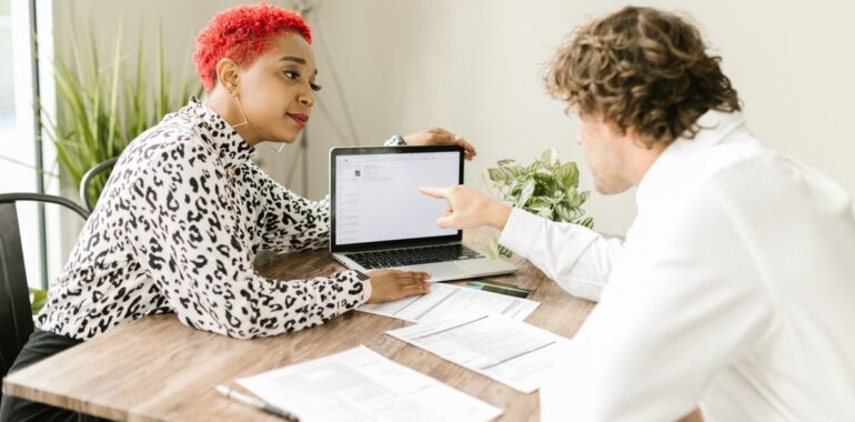 Deux collègues consultent un ordinateur portable et des documents sur une table de bureau