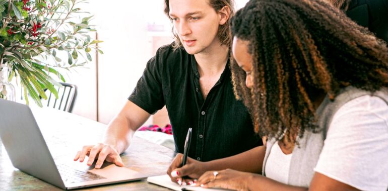 Deux collègues en réunion, l'une prend des notes à la main pendant que l'autre travaille sur un portable