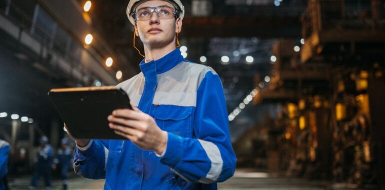 Technicien consultant une tablette sur un site industriel, illustrant un agent IA pour les rapports de service après intervention