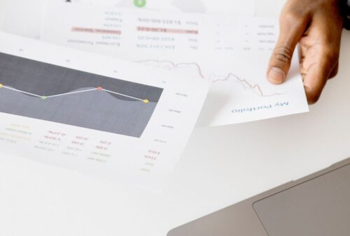 Main tenant des rapports imprimés avec graphiques à côté d'un ordinateur portable, comme un rapport hebdomadaire préparé par un agent IA