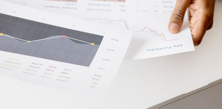 Main tenant des rapports imprimés avec graphiques à côté d'un ordinateur portable, comme un rapport hebdomadaire préparé par un agent IA