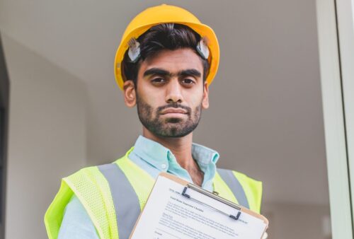 Entrepreneur en casque de chantier et dossard de sécurité tenant une planchette avec des documents