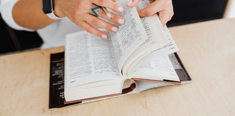 Mains feuilletant un dictionnaire sur un bureau en bois, illustrant un agent IA pour la traduction en entreprise