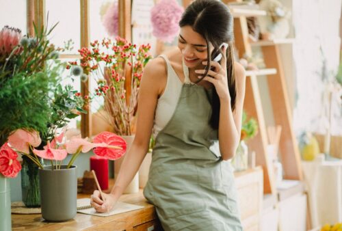 Propriétaire d’une boutique de fleurs qui parle au téléphone en prenant des notes derrière son comptoir