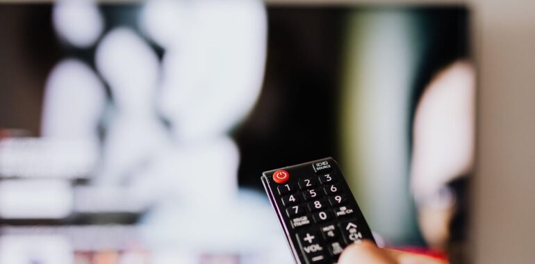 Main tenant une télécommande devant un téléviseur, illustrant la faille Plex dans les serveurs multimédias