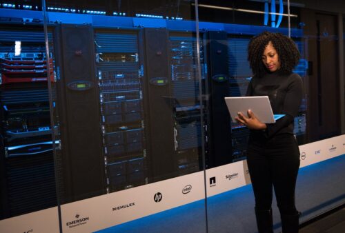 Professionnelle tenant un portable devant des baies de stockage de données, où dorment souvent de vieux feuillets de paie