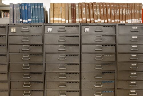 Rangée de classeurs métalliques gris surmontés de dossiers d'archives