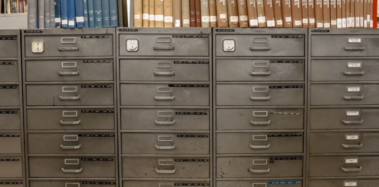 Rangée de classeurs métalliques gris surmontés de dossiers d'archives