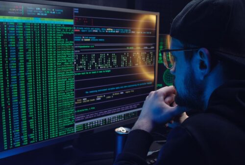 Personne en capuchon qui examine des lignes de code et de données sur un écran d'ordinateur