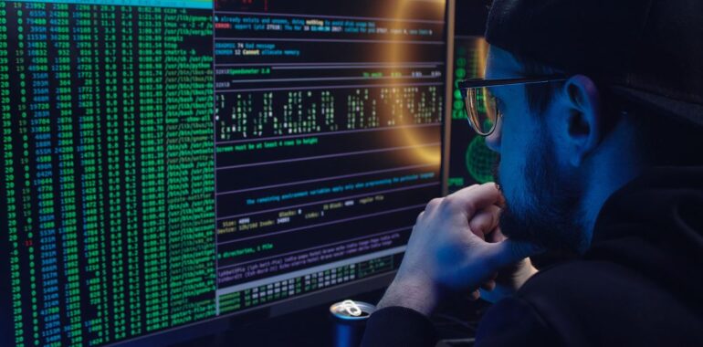 Personne en capuchon qui examine des lignes de code et de données sur un écran d'ordinateur