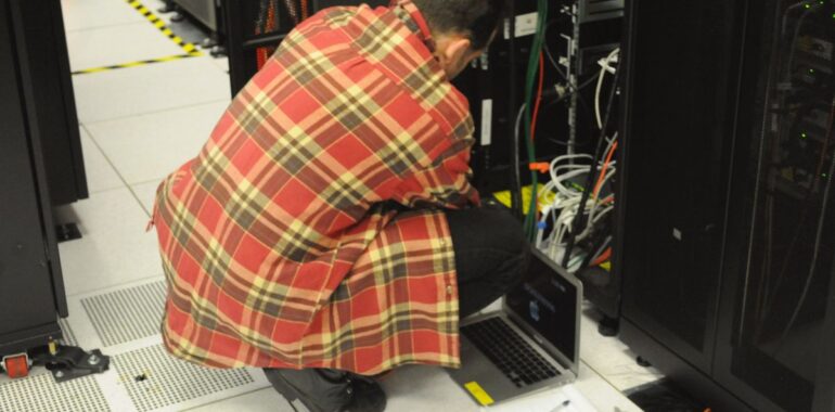 Technicien avec un ordinateur portable devant une baie de serveurs, comme les serveurs de sauvegarde visés par la faille AhsayCBS