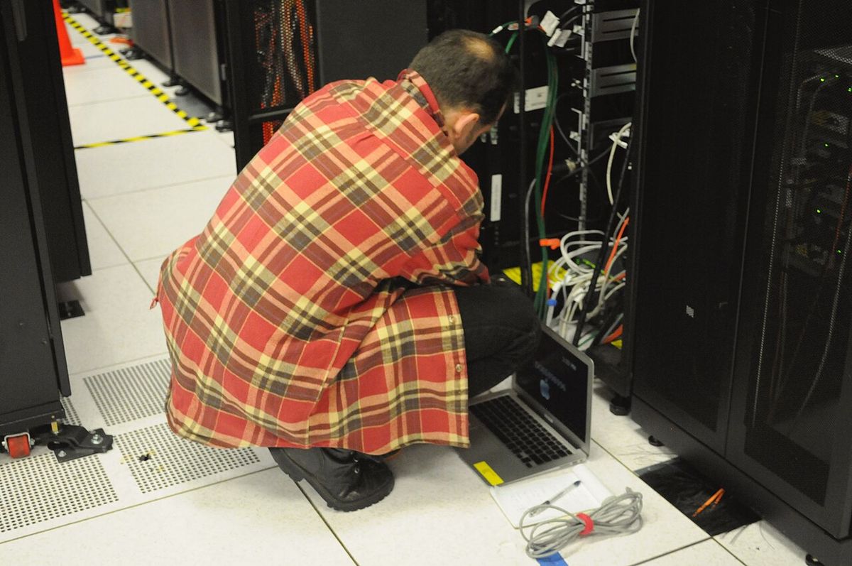 Technicien accroupi avec un ordinateur portable devant une baie de serveurs