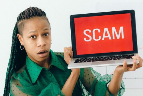 Femme surprise tenant un portable affichant SCAM, illustrant l'hameçonnage lié à Windows CVE-2026-96951