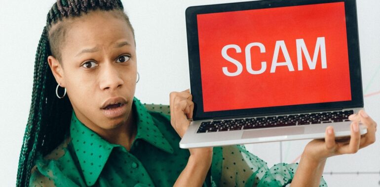 Femme surprise tenant un portable affichant SCAM, illustrant l'hameçonnage lié à Windows CVE-2026-96951